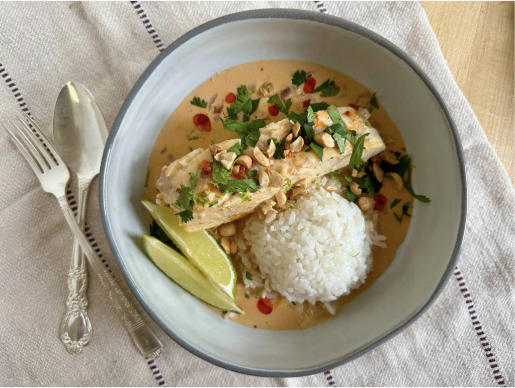 Round bowl with fish, rice, coral-colored curry broth and lime wedges